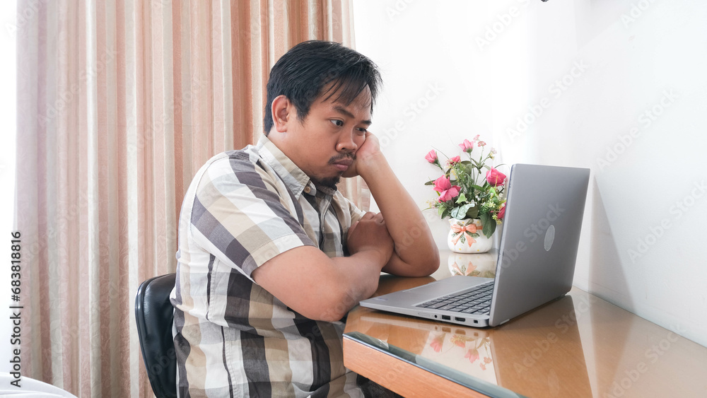 Indonesian man looking at laptop with disapproved and grumpy expression. Indonesian man looking at laptop with disapproved and grumpy expression.