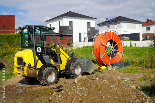 Roll of orange fiber optic cable for faster Internet in rural regions. Yellow digger for laying the underground cable in the soil. Barsinghausen, district of Hanover, Germany. photo