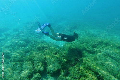 Girl snorkeling, skin diving and swimming with fins in the green blue sea, over the seabed. Activity in the water, seabed with rocks, underwater photography. Ocean with swimmer. 