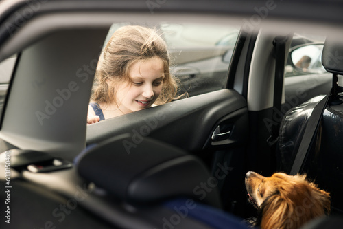 Little girl is looking through a window car to a cute little dog which is sitting inside the car