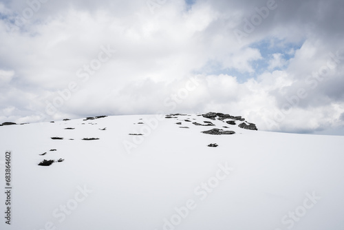 Perfect white snow on the mountain, against the black rocks and plants, on Kopren summit, under a moody, cloudy sky during winter