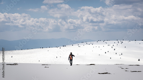Beautiful snow covered mountain highlands and a mountain hiker with orange backpack
