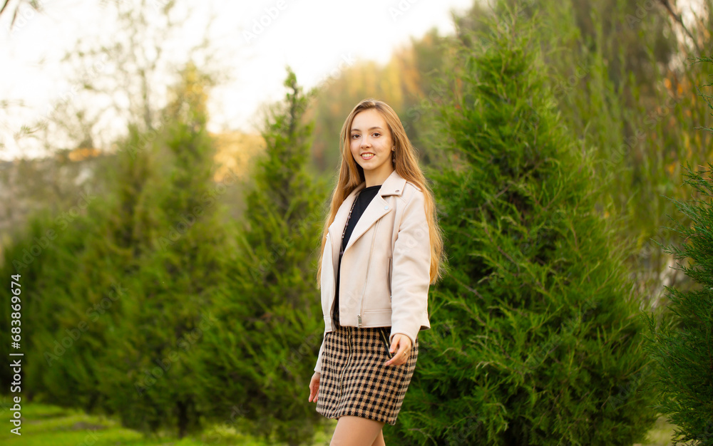 A young smiling girl walking in an autumn park in a good mood. Teenage girl, portrait against a background of nature. Fashion style trend. A young smiling girl walking in an autumn park in a good mood. Teenage girl, portrait against a background of nature. Fashion style trend.