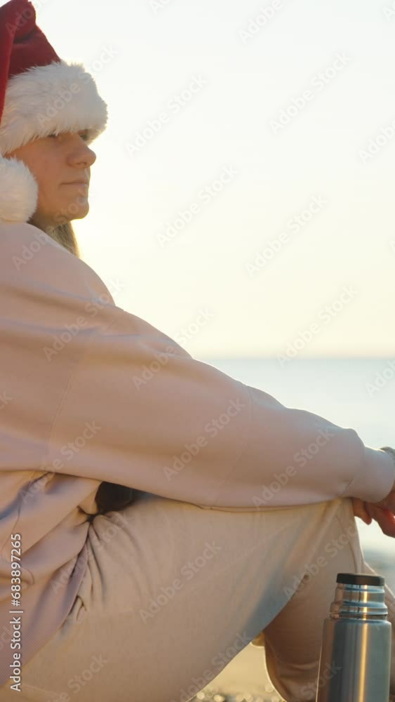 Vertical video. A young woman in a red Santa hat welcomes the sunrise ...