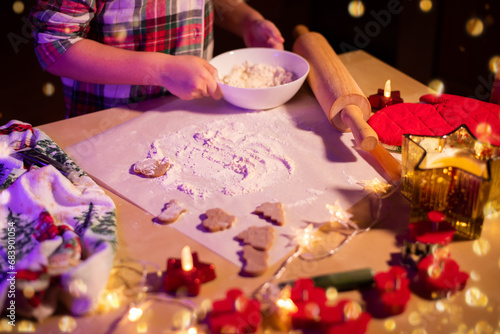 Children's hands covered in flour prepare Christmas cookies against the background of a festively decorated table.