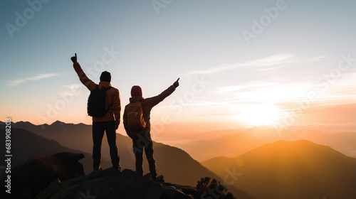 Two Hikers Celebrating Sunset Atop Mountain with Silhouettes Against Vivid Sky