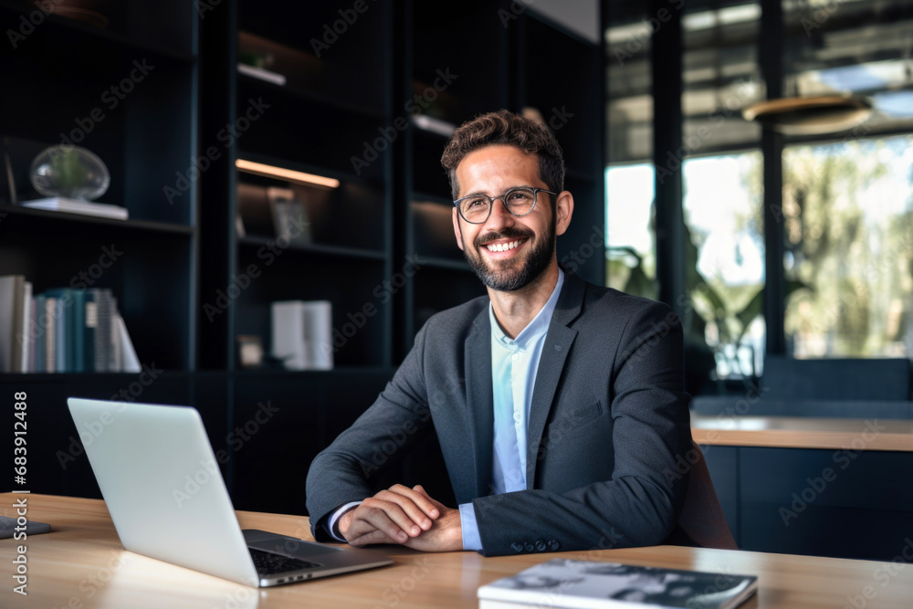 Happy businessman smiling at camera while working on laptop in office. Happy businessman smiling at camera while working on laptop in office.