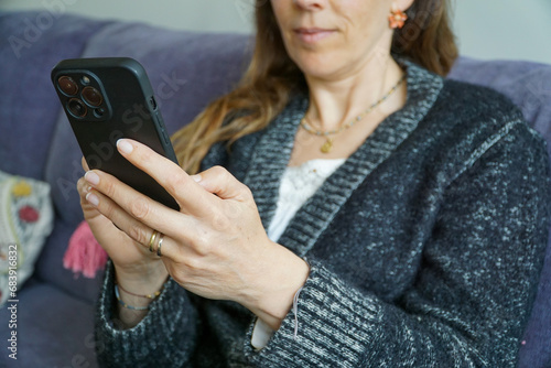 50 year old woman typing on her phone while sitting on her couch.