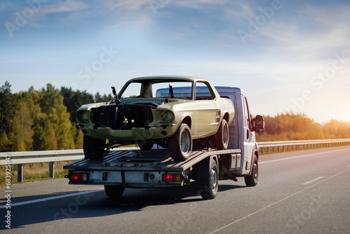 A Towing Truck In Motion With A Damaged Car After The Traffic Accident On A Road. Emergency Roadside Assistance. Retro Car Project Renovation. Vintage Car Recovery And Reanimation. photo