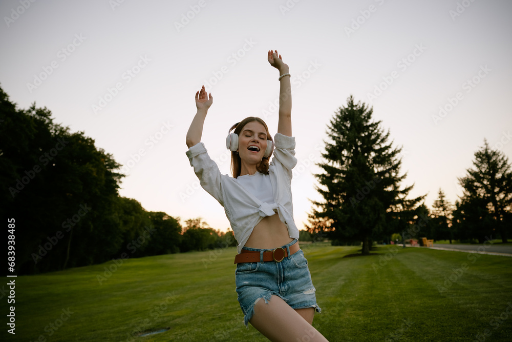 Happy teenage woman wearing headphones dancing on park lawn Happy teenage woman wearing headphones dancing on park lawn