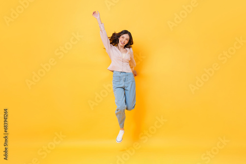 Cheerful Asian woman in casual clothes smiling and jumping with hand up in colorful yellow color isolated background studio shot photo