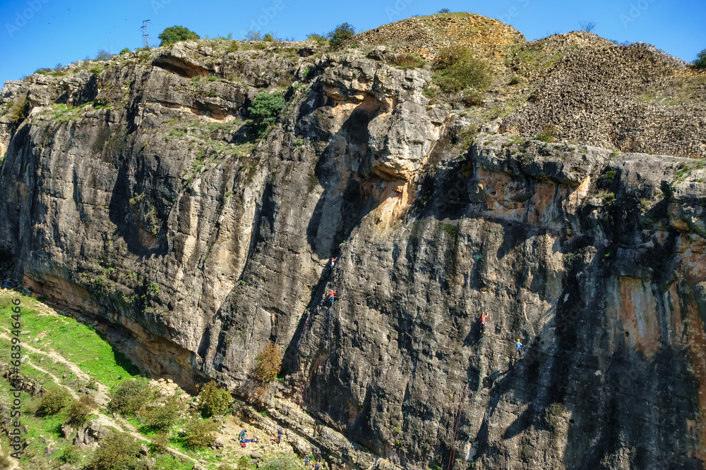 Climbers climbing a vertical rock wall in the valley of Ponton de la Oliva, Madrid.