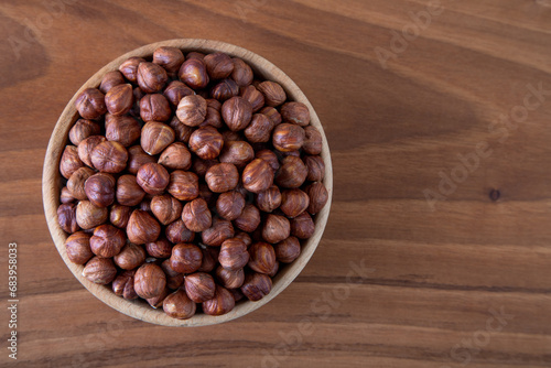 Top view of a bowl full of peeled hazelnuts on wooden table 