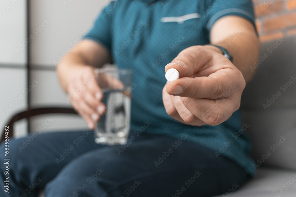 Man taking medicine, holding in a hand white therapeutic pill, antibiotics, painkiller and glass of water, close-up view