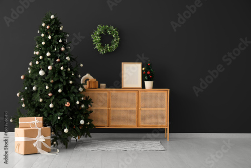 Beautiful Christmas tree with gifts and wooden dresser near dark wall. Banner for design photo