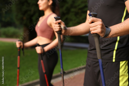 Couple practicing Nordic walking with poles outdoors, selective focus