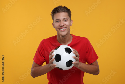 Happy sports fan with soccer ball on orange background © New Africa