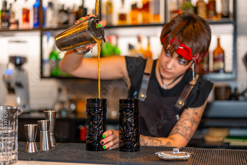 Alternative young bartender pouring cocktail into a creative glass