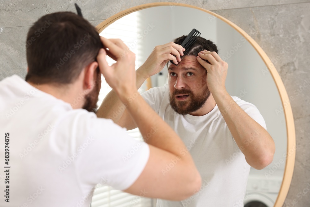 Dandruff problem. Man with comb examining his hair and scalp near mirror indoors Dandruff problem. Man with comb examining his hair and scalp near mirror indoors