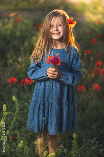 Obraz na płótnie little girl in blue dress on sunset ni poppy seed red flowers green grass summer field bloom cute alone w salonie