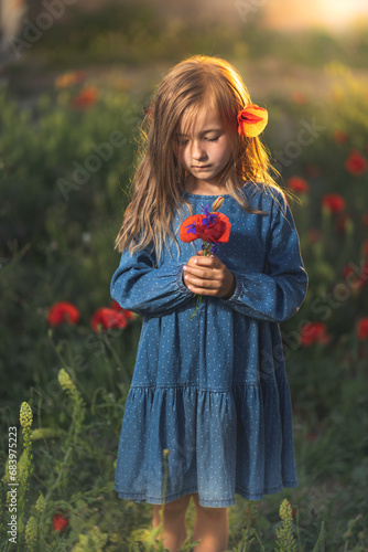 Obraz na płótnie little girl in blue dress on sunset ni poppy seed red flowers green grass summer field bloom cute alone w salonie