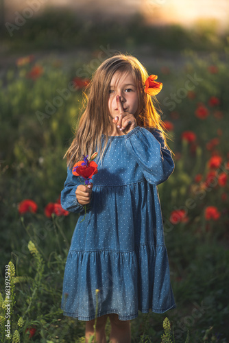 Obraz na płótnie little girl in blue dress on sunset ni poppy seed red flowers green grass summer field bloom cute alone w salonie