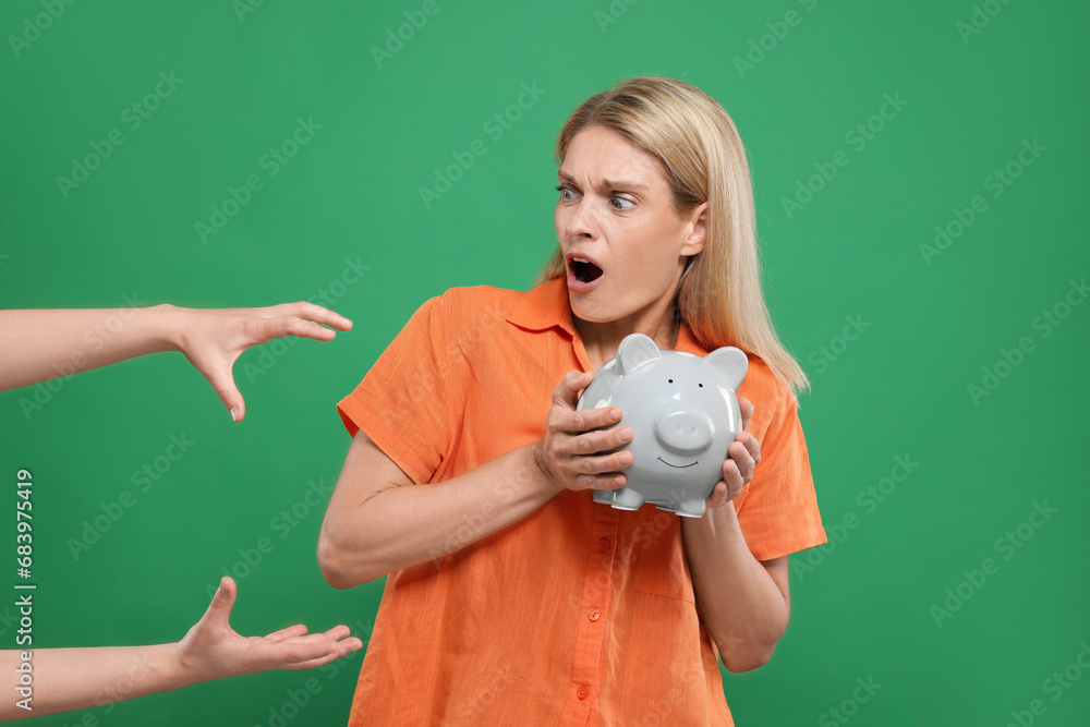 Scammer taking piggy bank from emotional woman on green background. Be careful - fraud Scammer taking piggy bank from emotional woman on green background. Be careful - fraud