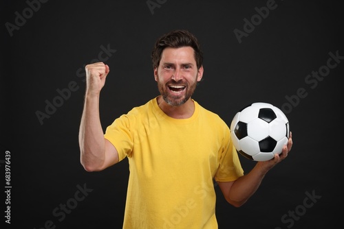 Emotional sports fan with soccer ball on black background
