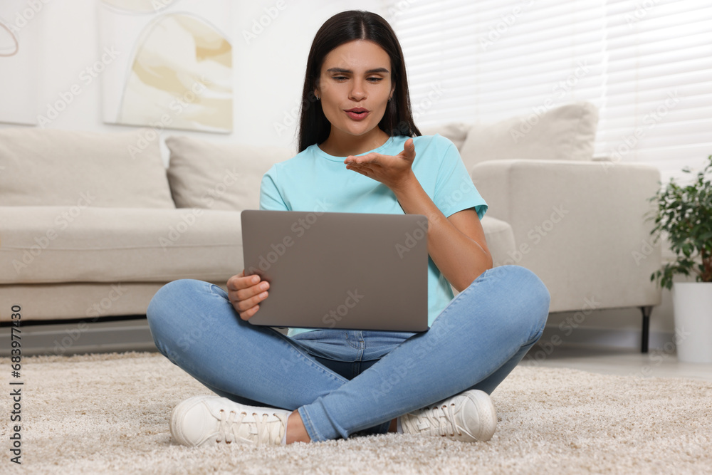Young woman having video chat via laptop and blowing kiss on floor at home Young woman having video chat via laptop and blowing kiss on floor at home