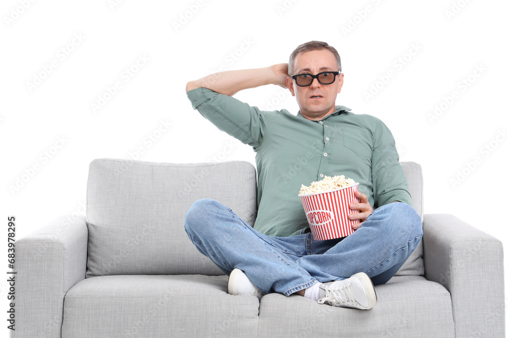 Scared mature man in 3D glasses with popcorn watching movie on sofa against white background