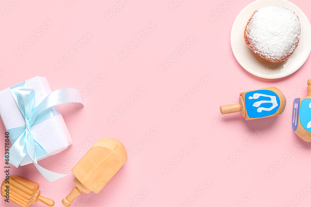 Hanukkah composition with dreidels, donut and gift box on pink background