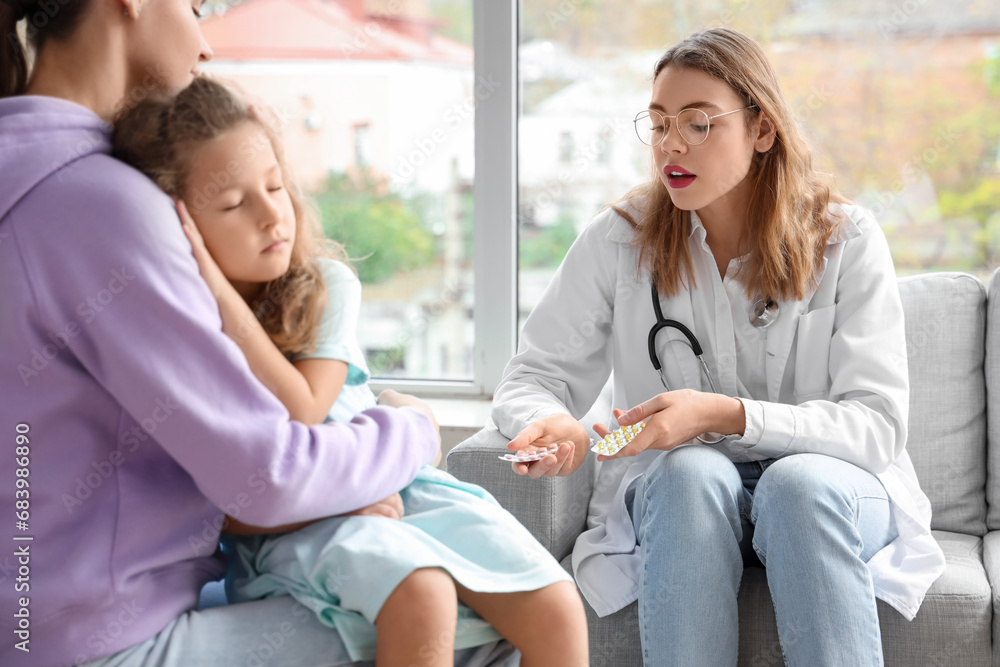 Female doctor giving pills to ill little girl with mother at home Female doctor giving pills to ill little girl with mother at home