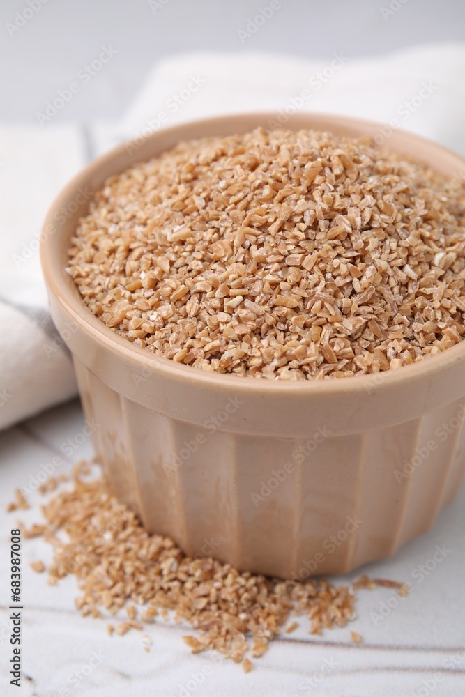 Dry wheat groats in bowl on white textured table, closeup Dry wheat groats in bowl on white textured table, closeup