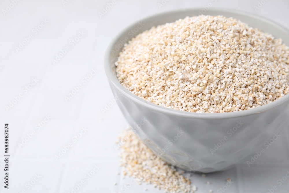 Dry barley groats in bowl on white tiled table, closeup. Space for text Dry barley groats in bowl on white tiled table, closeup. Space for text