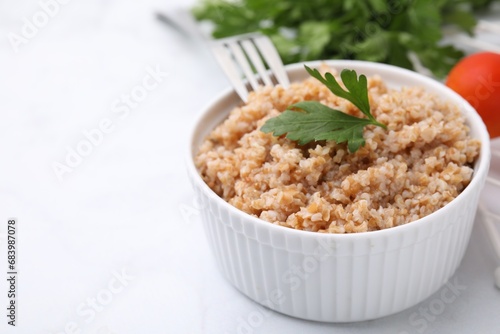 Tasty wheat porridge with parsley in bowl on white table, closeup. Space for text photo