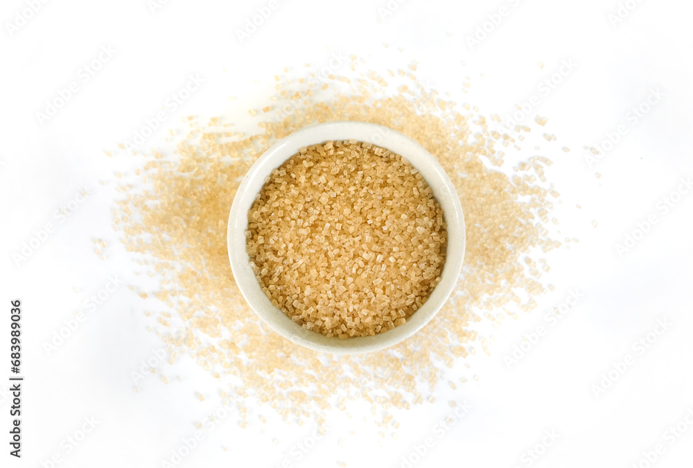 Small bowl of raw brown sugar with scattered crystals on white background Small bowl of raw brown sugar with scattered crystals on white background