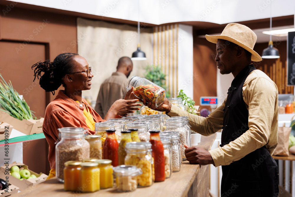 Friendly African American male vendor advising and assisting a black woman with fresh pasta suggestions. The store offers organic produce, bulk items, and plastic-free packaging.
