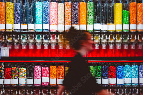 A woman walks past a wall of candy dispensers, motion blurred