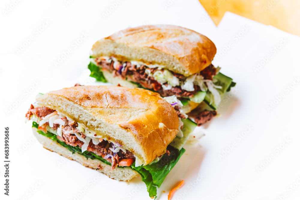 Two halves of a roast beef sandwich on white paper Two halves of a roast beef sandwich on white paper