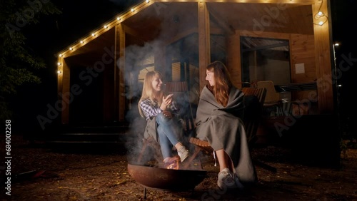 girl friends laughing and kissing sitting by the fire in the evening in country hotel in the woods