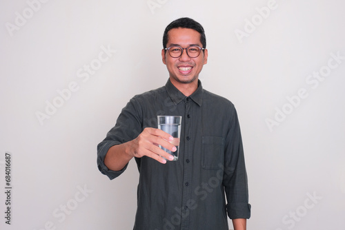 Adult Asian man smiling happy while offering a glass of water photo