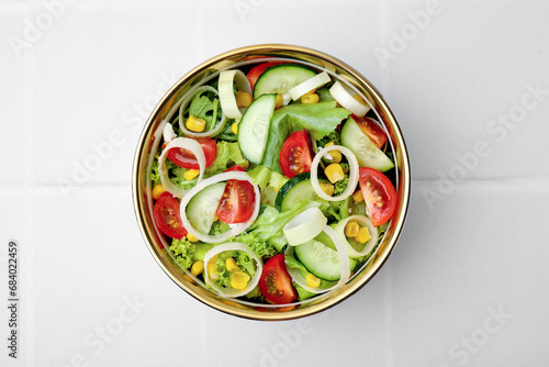 Bowl of tasty salad with leek, tomatoes and cucumbers on white tiled table, top view