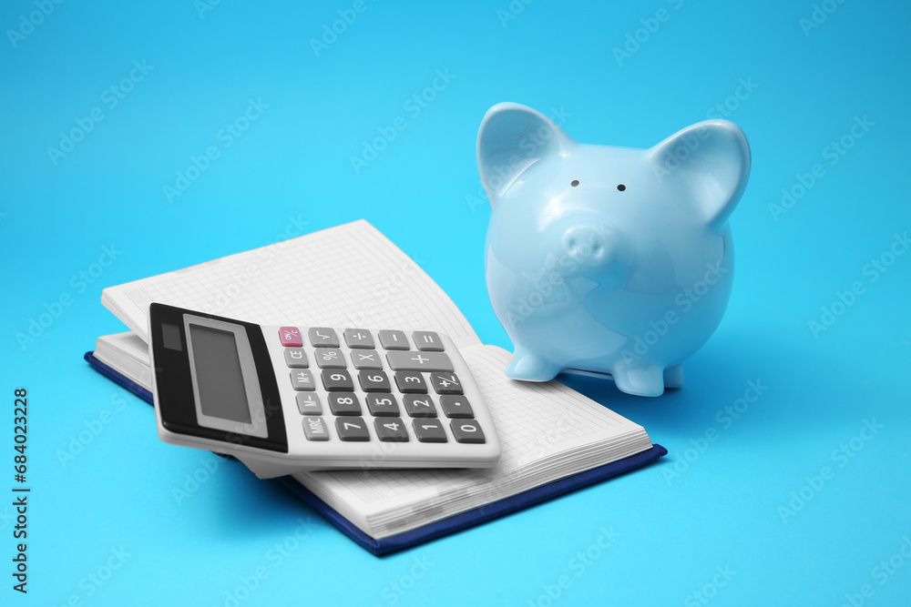 Piggy bank, notebook and calculator on light blue background Piggy bank, notebook and calculator on light blue background