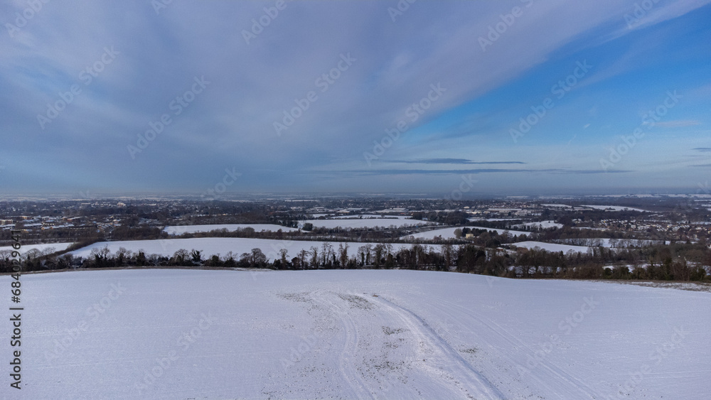 Aerial view of the picturesque English countryside blanketed in snow during winter. The drone captures the serene beauty of snow-covered fields, with the intricate patterns of the landscape highlighte