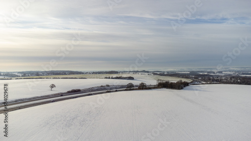 Aerial view of the picturesque English countryside blanketed in snow during winter. The drone captures the serene beauty of snow-covered fields, with the intricate patterns of the landscape highlighte
