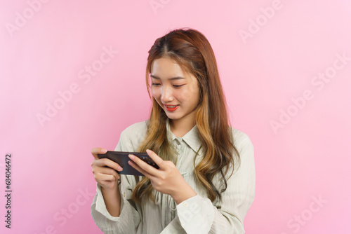 Young women smiling and playing video game on smartphone isolated on pink background