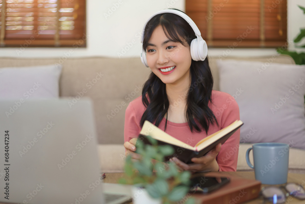 Young businesswoman wear headphone to meeting in video call on laptop and writing notes in notebook Young businesswoman wear headphone to meeting in video call on laptop and writing notes in notebook