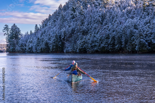 Canvas Print two young women paddling a green canoe on a river with trees clad in freshly fal