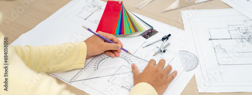 Cropped image of professional architect designer hand draws blueprint while project manager shows the mistake point with architectural document, color palette scatter around. Closeup. Variegated.