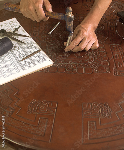 Bild auf Leinwand Hands of an artisan embossing a leather-covered table with a hammer and burin